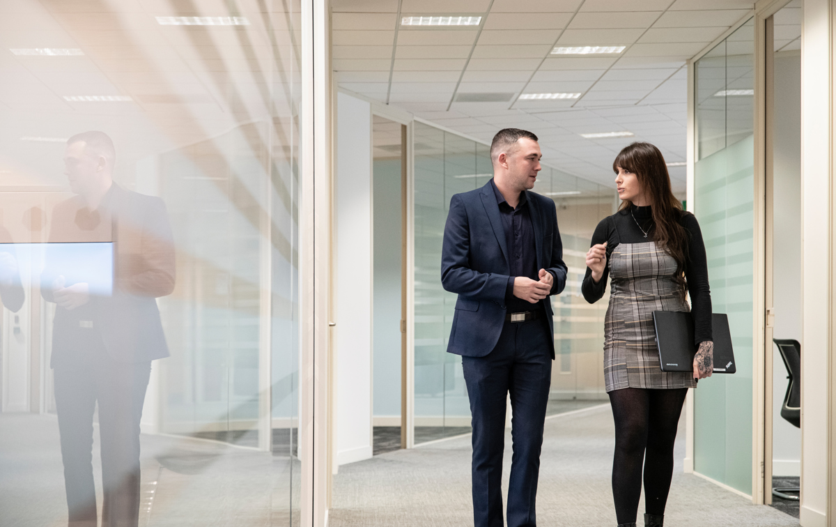 Mann og kvinne går sammen nedover korridoren, illustrasjon av to ansatte i Intrum som jobber med bank og finans.